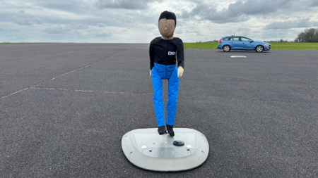 The child pedestrian dummy for ADAS testing, standing on a test track wearing a black shirt and blue trousers