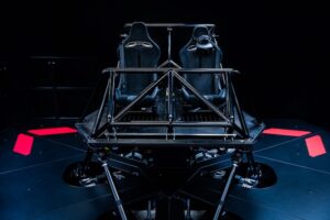 Dynisma DMG-X driving simulator with dual racing seats mounted on a hexapod motion platform with pink accent panels against a dark background