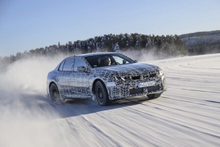 The BMW i3 being tested on frozen lake surfaces near Arjeplog, Sweden. The silver car is being driven fast, throwing up snow and ice